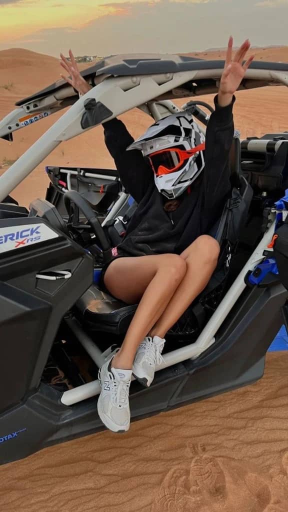 Rider in a Can-Am Maverick buggy on sand dunes at sunset